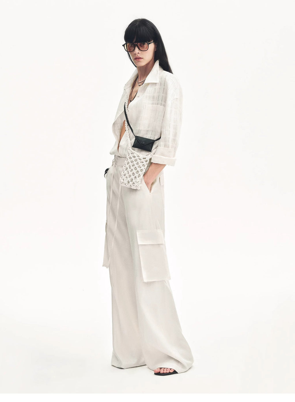"Rhythm in the Same Frequency" white linen cargo pants worn with a white shirt and woven bag, side view