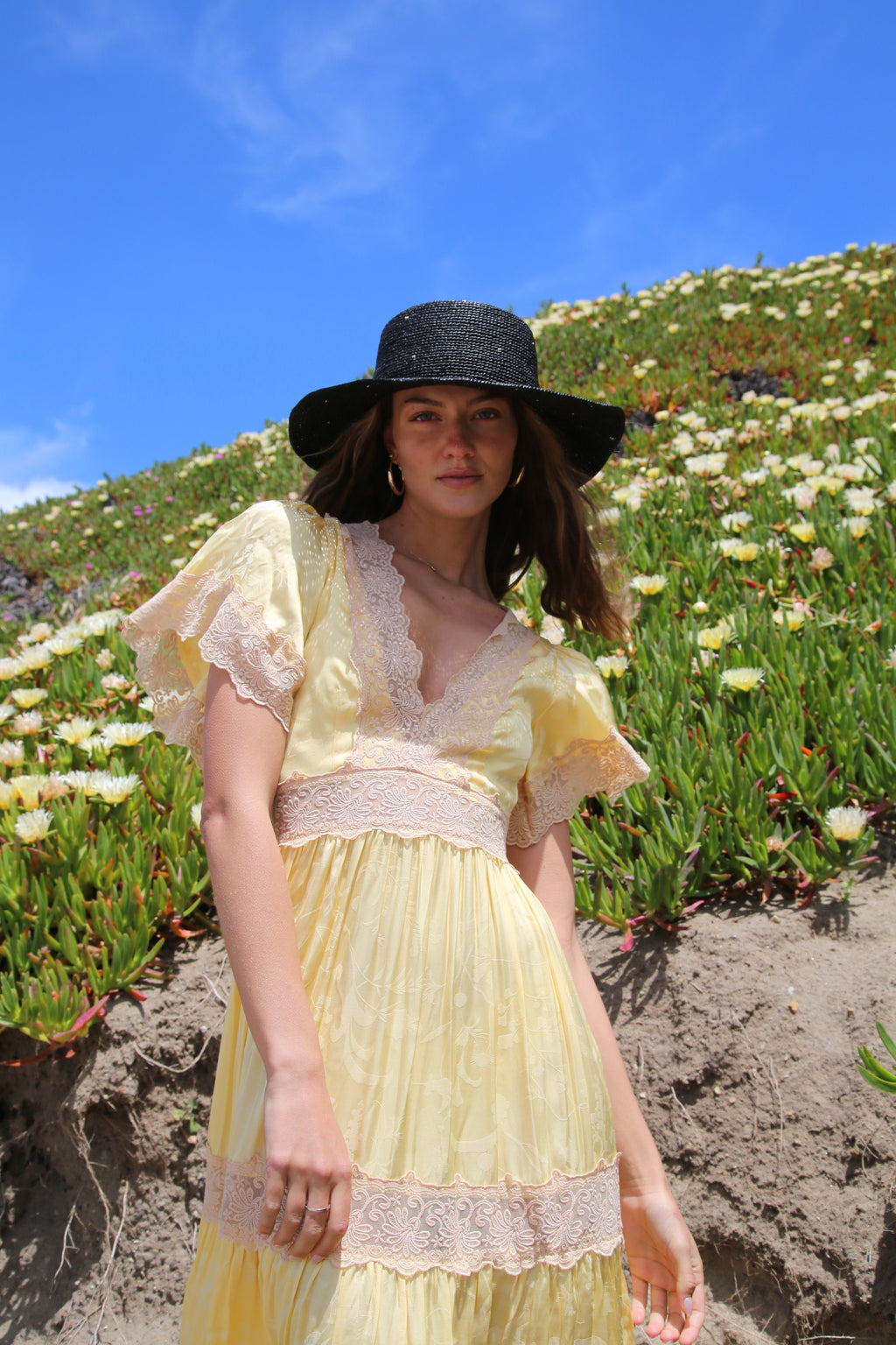 Resort Collection black raffia hat styled with a yellow ruffled dress on a hillside